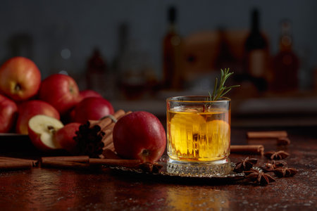 Apple kombucha with apple slices and a rosemary sprig. Fresh apples, cinnamon sticks, and anise are scattered on an old kitchen table.の写真素材