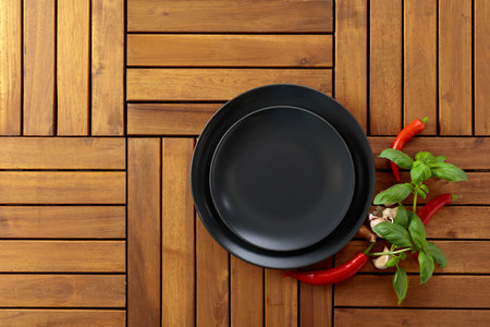 Empty black plate, garlic, basil, and red pepper on a natural wooden background. Soft, diffused light from top left. Place your product on the plate. Copy space.の写真素材