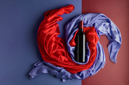 Bottle of red wine against a background of draped red and blue silk fabric. Top view.の写真素材