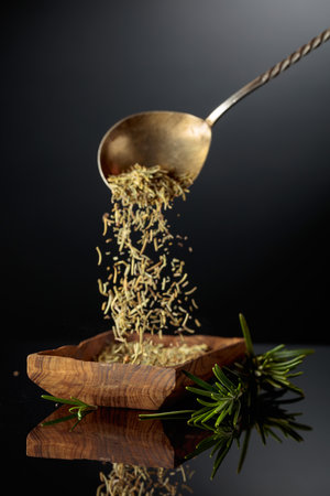 Rosemary on a black reflective background. Dry rosemary are poured into a wooden bowl.の写真素材