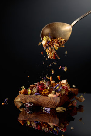 Various dried herbs and spices are poured into a wooden dish. Black reflective background.の写真素材