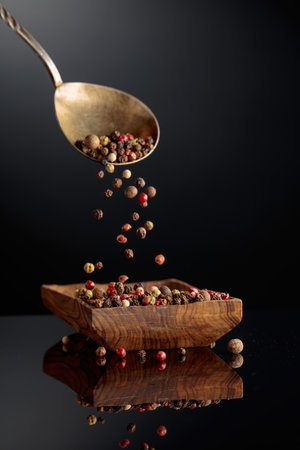 Peppercorn mix on a black background. Black, red, white, and allspice peppercorns are poured in wooden dish.の写真素材