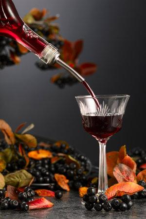 Black chokeberry liqueur is poured from a bottle into a glass. Sweet flavor drink and fresh berries...