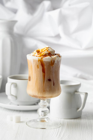 Iced caramel latte topped with whipped cream and caramel sauce, refreshing and sweet coffee drink on a white table.の写真素材