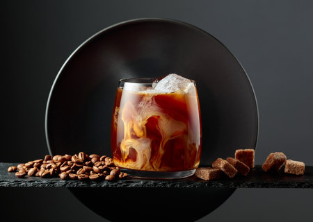Iced coffee with cream on a black background. Iced drink with coffee beans and brown sugar.の写真素材