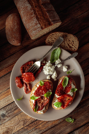 Ciabatta with sun dried tomatoes in olive oil, ricotta, and basil. Traditional Italian snack on an old wooden table. Top view.の写真素材