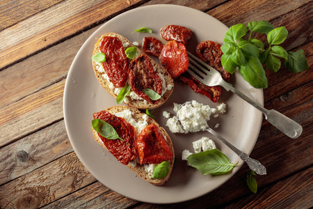 Ciabatta with sun dried tomatoes in olive oil, ricotta, and basil. Traditional Italian snack on an old wooden table. Top view.の写真素材