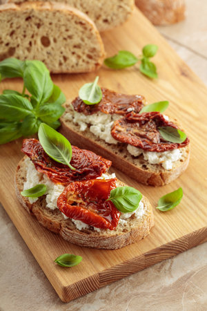 Ciabatta with sun dried tomatoes in olive oil, ricotta, and basil. Traditional Italian snack on a wooden cutting board.の写真素材