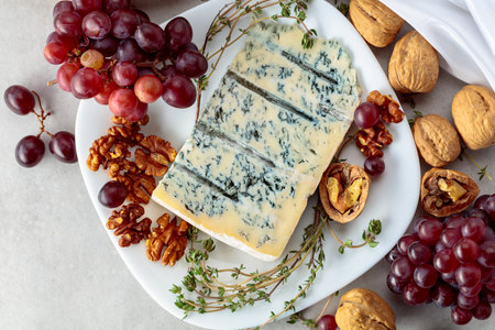 Gorgonzola cheese with walnuts, red grapes, and thyme on a white kitchen table. Top view.