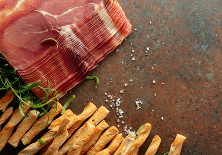 Prosciutto with bread sticks and rosemary on a brown rusty background. Top view.の写真素材