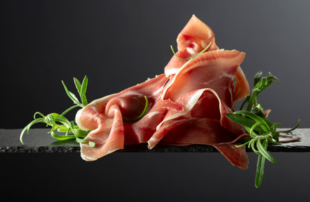 Prosciutto crudo with rosemary on a black background. Copy space.の写真素材