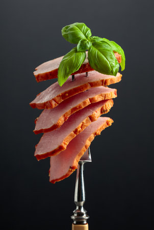 Sliced smoked ham with basil on a fork.の写真素材