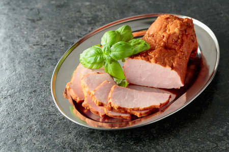 Delicious sliced smoked ham with basil on a metal tray.
