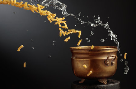 Vintage brass pot and fusilli pasta with a splash of water in motion. Concept of Italian food. Copy space.の写真素材