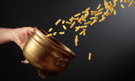 Vintage brass pot and fusilli pasta in motion. Concept of Italian food. Copy space.の写真素材