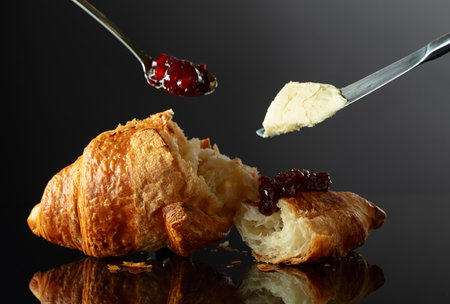 Fresh baked croissant with butter and raspberry jam on a black reflective background.の写真素材