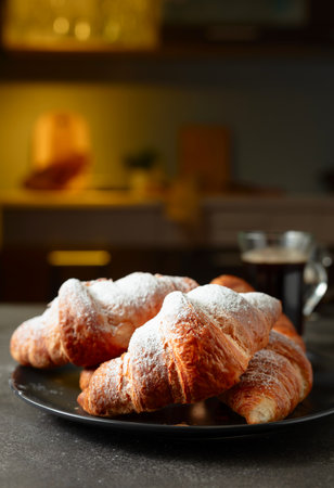 Fresh baked croissants and black coffee on a kitchen table. Croissants sprinkled with sugar powder. Selective focus.の写真素材