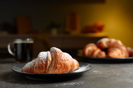 Fresh baked croissants and black coffee on a kitchen table. Croissants sprinkled with sugar powder. Selective focus.の写真素材