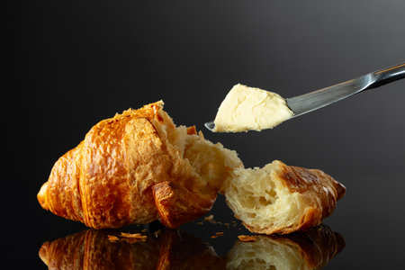 Fresh baked croissant with butter on a black reflective background.の写真素材