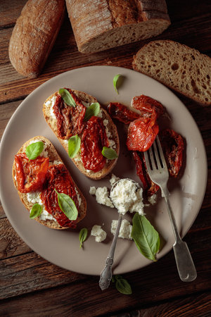 Ciabatta with sun dried tomatoes in olive oil, ricotta, and basil. Traditional Italian snack on an old wooden table. Top view.の写真素材