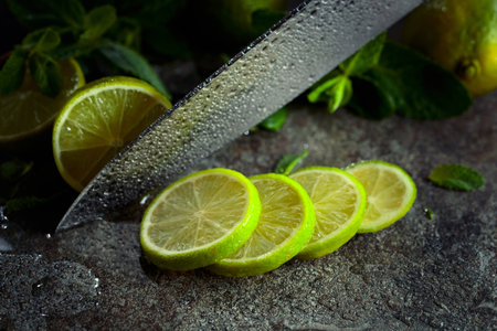 A knife, slices of lime and sprigs of fresh mint on a wet stone table.