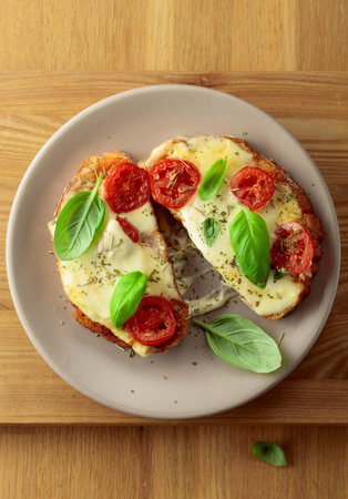 Delicious hot open sandwiches with mozzarella cheese, tomatoes, basil and spices on a wooden table.の写真素材