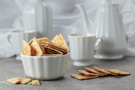 Crunchy square crackers and black coffee. Gray stone table and white utensils.