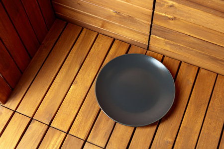 Empty black plate on natural wooden background. Soft, diffused light from top left. Place your...