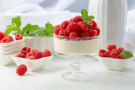 Mascarpone cream with fresh raspberries in a clear bowl on a white wooden table. Berry parfait...