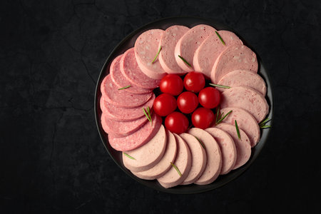 Various boiled sausages with tomatoes and rosemary on a black plate. Top view. Black background with copy space.の写真素材