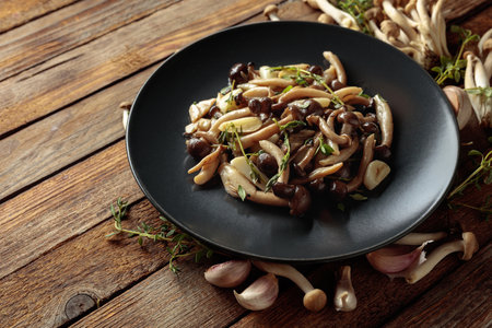 Fried shimeji mushrooms with thyme and garlic on a black plate. Fresh and prepared mushrooms with ingredients. Traditional Japanese cuisine.の写真素材