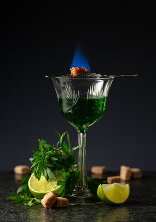 Burning sugar on a glass with absinthe. Preparation of the drink. Absinthe with ingredients on a...