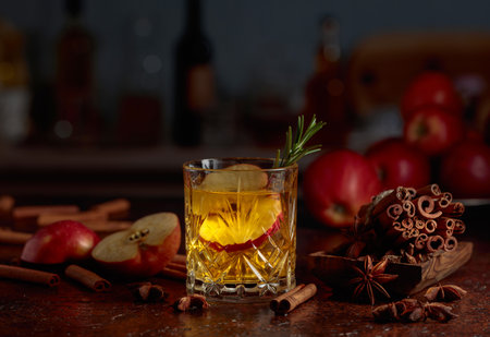 Apple kombucha with apple slices and a rosemary sprig. Fresh apples, cinnamon sticks, and anise are scattered on an old kitchen table.の写真素材