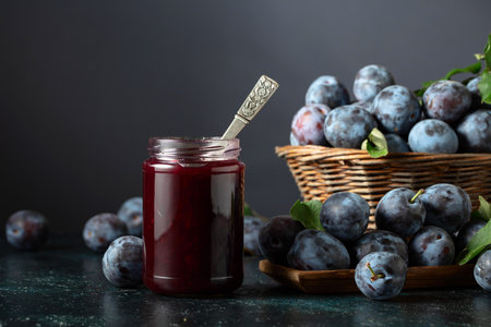 Plum jam and fresh berries on a dark blue background. Ripe plums with jam on the kitchen table.