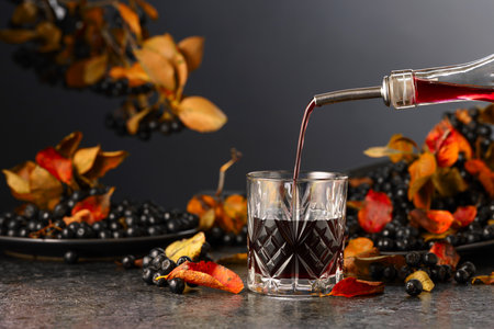 Black chokeberry juice and fresh berries on a black background. Juice is poured from a bottle into a glass.の写真素材