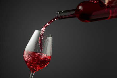 Pouring pink wine from a bottle into a glass. Gray background with copy space.の写真素材