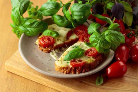 Delicious hot open sandwiches with mozzarella cheese, tomatoes, basil and spices on a wooden table.の写真素材