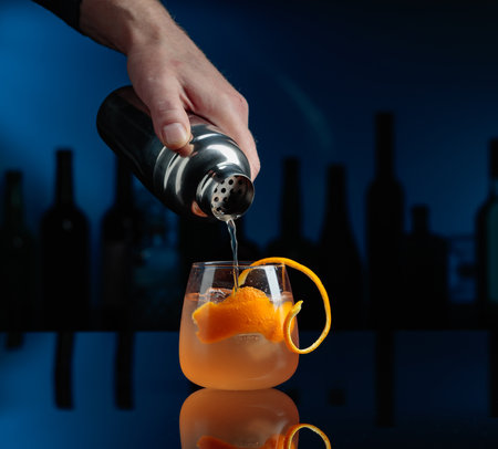 Cocktail Auld Draper on a black reflective background. The bartender pours a cocktail from a shaker...