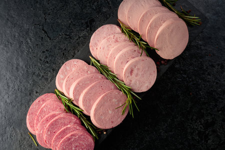 Various boiled sausages with rosemary on a black stone background.