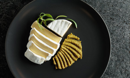 Camembert cream cheese with pesto on a black plate. Top view.