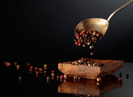 Peppercorn mix on a black background. Black, red, white, and allspice peppercorns are poured in...