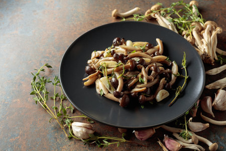 Fried shimeji mushrooms with thyme and garlic on a black plate. Fresh and prepared mushrooms with...