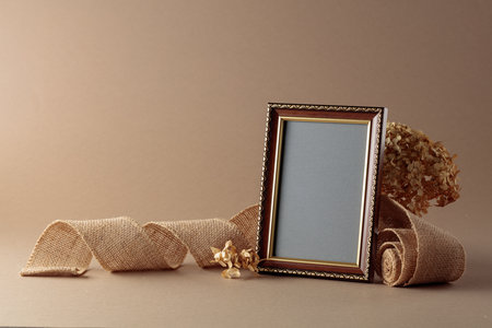 Empty picture frame, burlap ribbon and dried hydrangea flowers on beige background. Place your image...