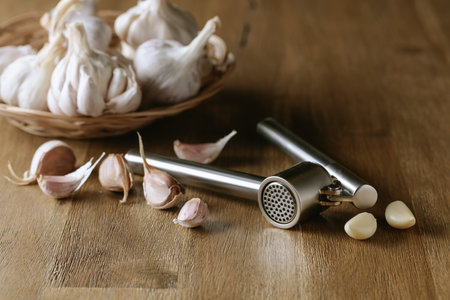Garlic bulbs and garlic press on an old wooden table.