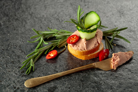 Bread slices with pate, cucumber, red pepper, and rosemary. Black background with copy space.