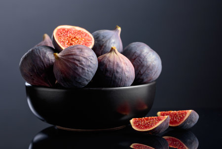 Fresh fig fruit with juicy red pulp. Ripe fig fruit in black dish on a black reflective background. Delicious fruit sliced open, and healthy rich in nutrients.の写真素材