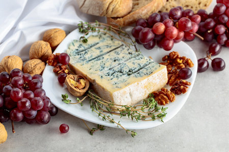 Gorgonzola cheese with walnuts, red grapes, and thyme on a white kitchen table.