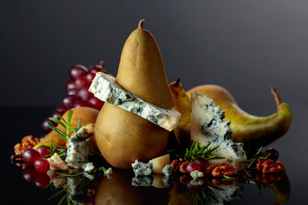 Blue cheese with pear, walnuts, red grapes, and rosemary. Tradition blue mold cheese with fruits on a black reflective background. Copy space.の写真素材
