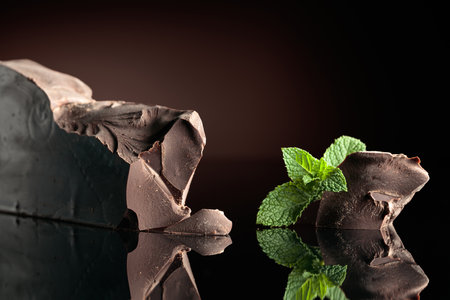 Large piece of dark bitter chocolate with mint on a black reflective background.の写真素材