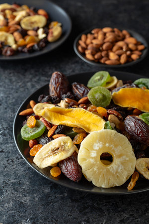 Dried tropical fruits, nuts, and raisins on a black stone table.の写真素材